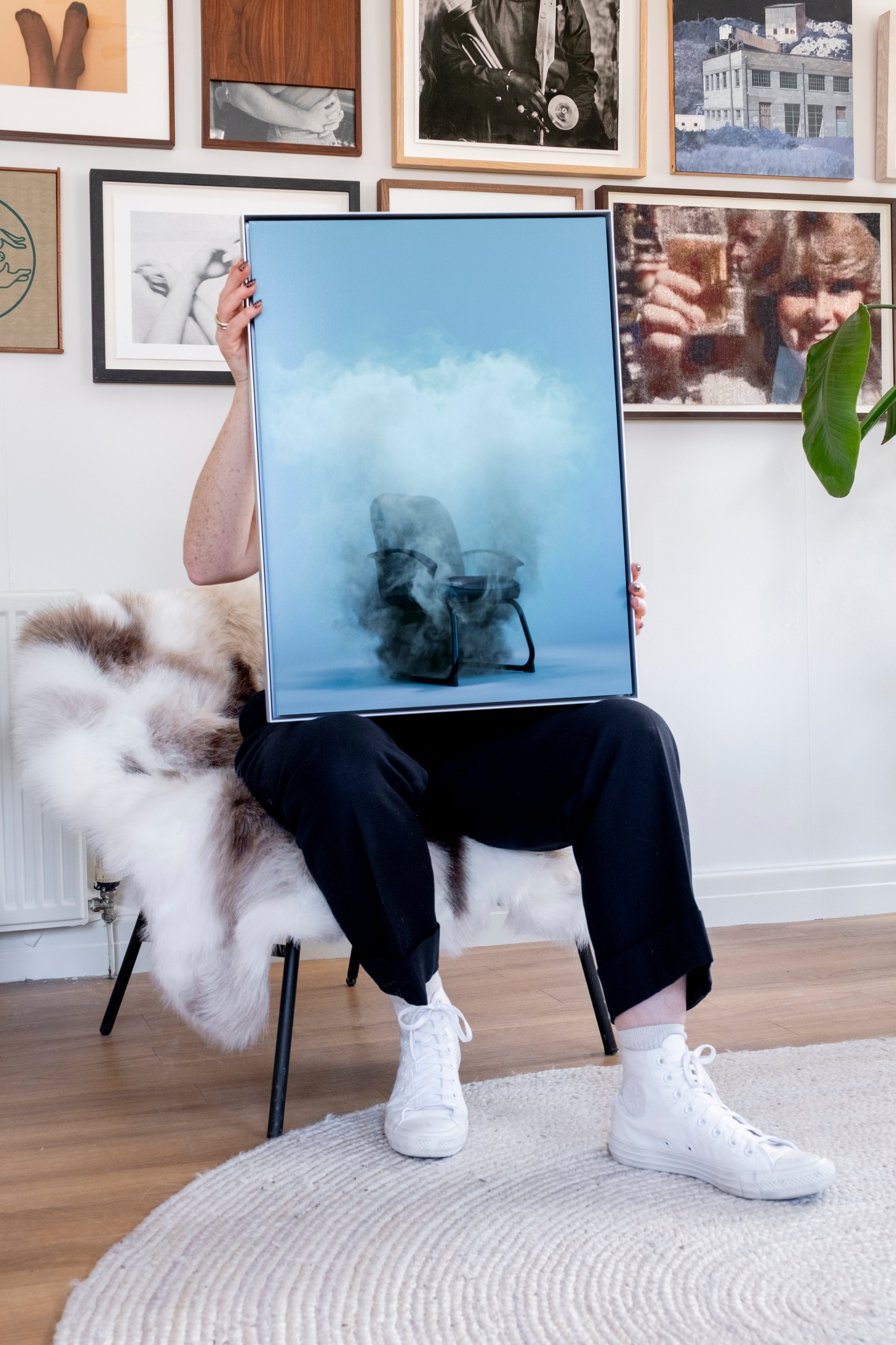 Person holding a framed artwork in a room with framed pictures on the wall.