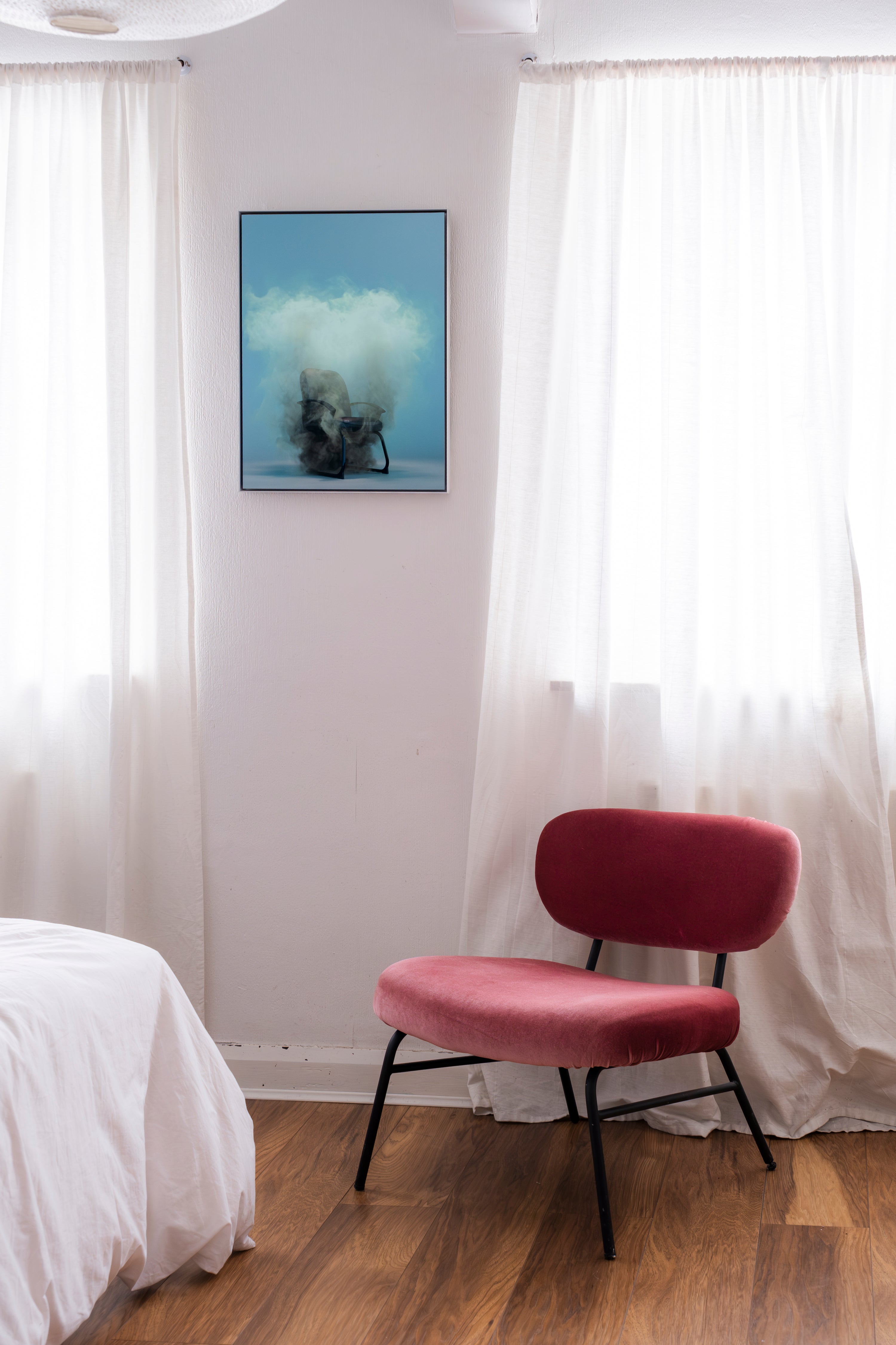 Red chair in a room with white curtains and a framed picture on the wall.