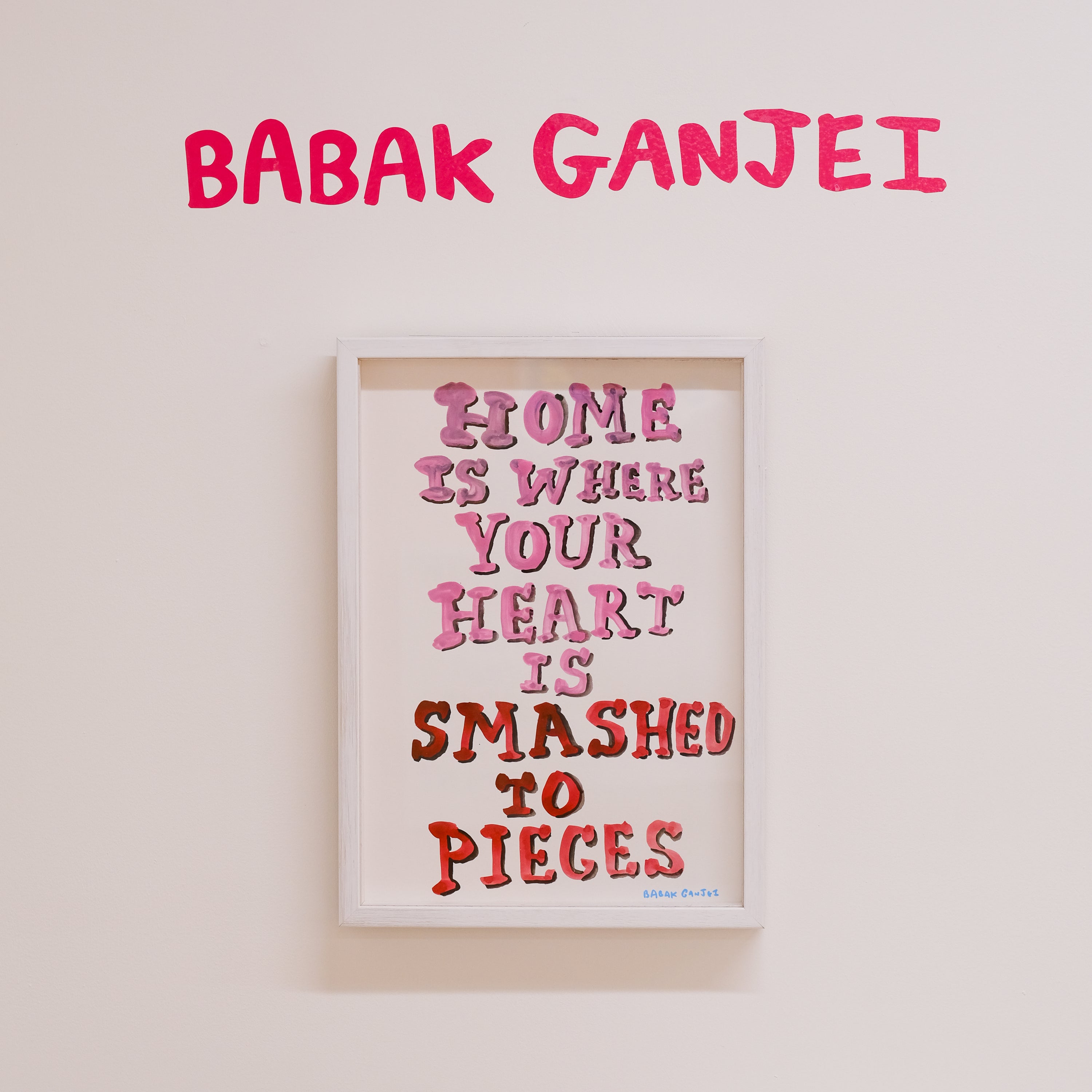 Framed artwork with text 'Home is where your heart is smashed to pieces' by Babak Ganjei on a light background