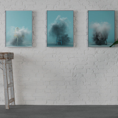 Three blue artworks on a white brick wall with a plant and stools in the foreground.